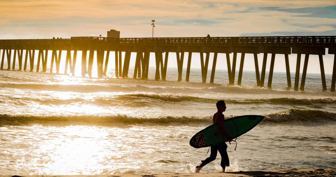Surfer carrying a surfboard on Panama City Beach during sunset