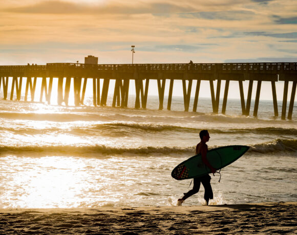 Surfer carrying a surfboard on Panama City Beach during sunset