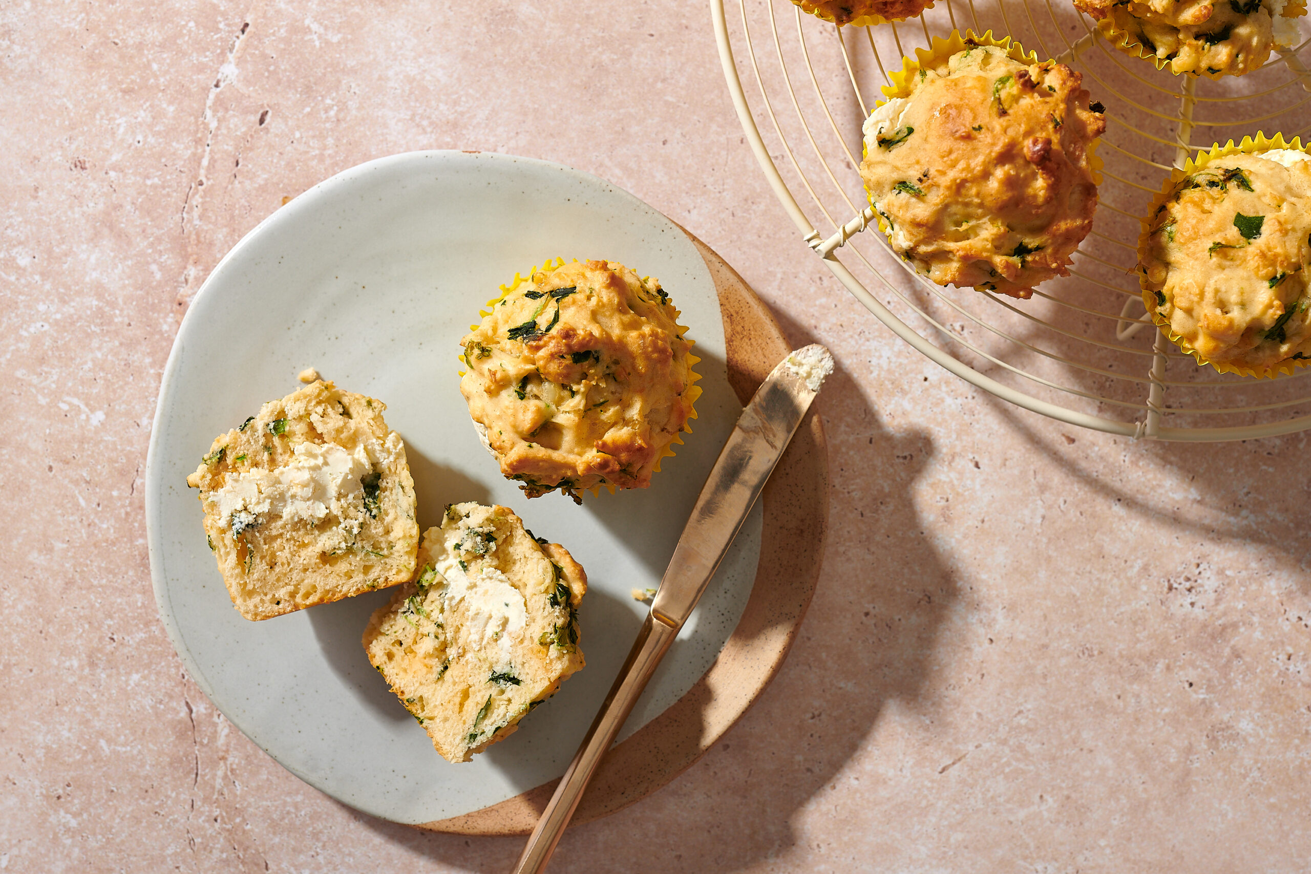 Savoury muffins with a cream cheese centre - photo of two muffins on a plate, one is cut open to reveal the centre, with some muffins on a cooling rack in the background