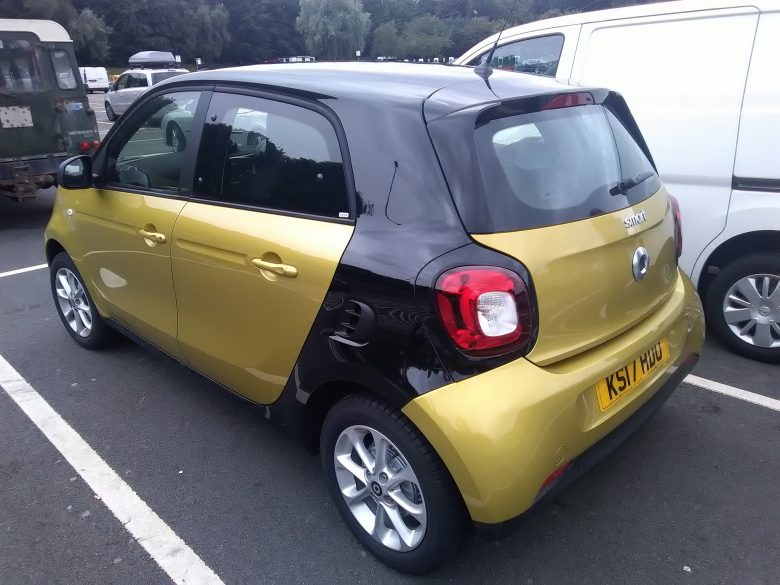 Yellow and black Smart car parked in a car park