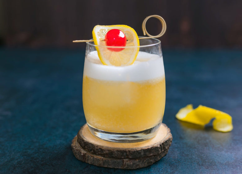 Photo of a whiskey sour cocktail with a cherry and lemon slice garnish