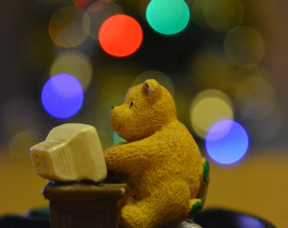 Toy teddy bear sitting at a computer