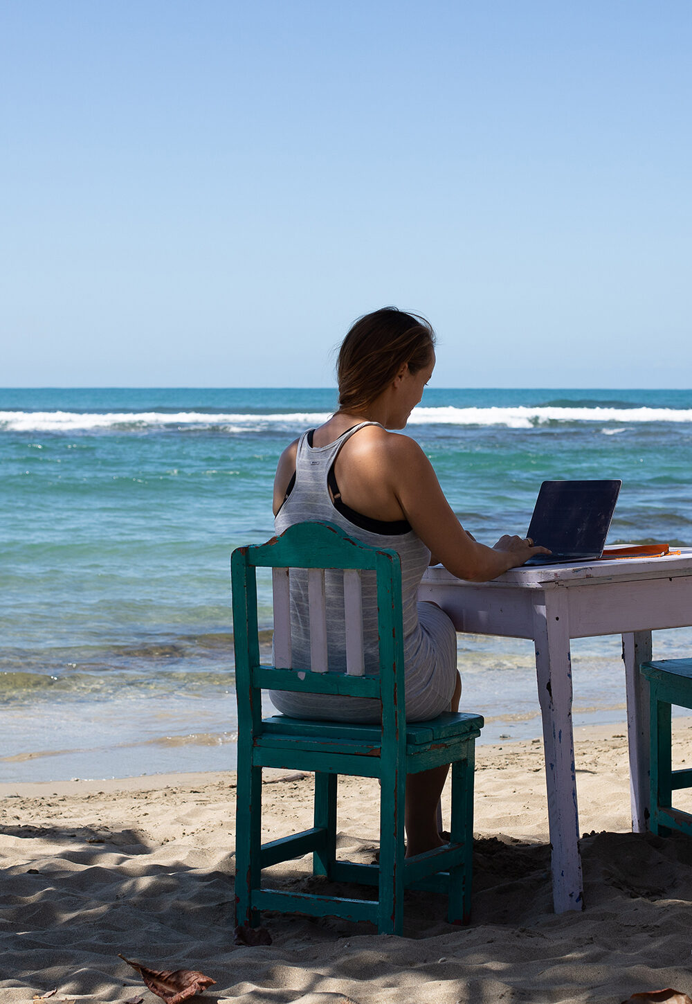 Woman working on a laptop at a table on the beach