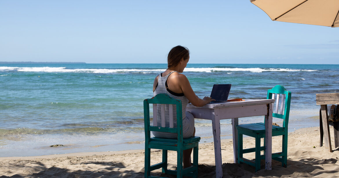 Woman working on a laptop at a table on the beach