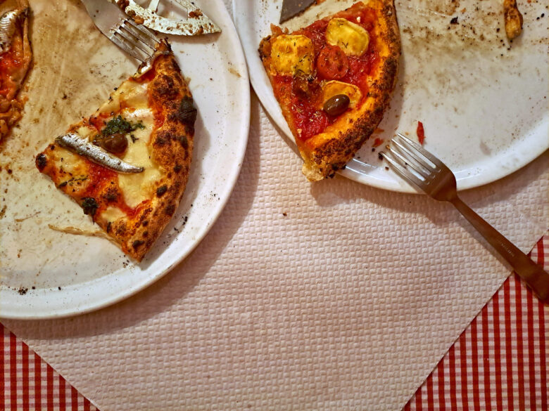 An overhead shot of two plates of half-eaten pizza served on a red checked tablecloth at Pizzeria Chez Sauveur, Marseille