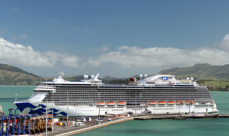 A Princess Cruises ship docked in port, surrounded by blue water and with gorgeous scenery behind