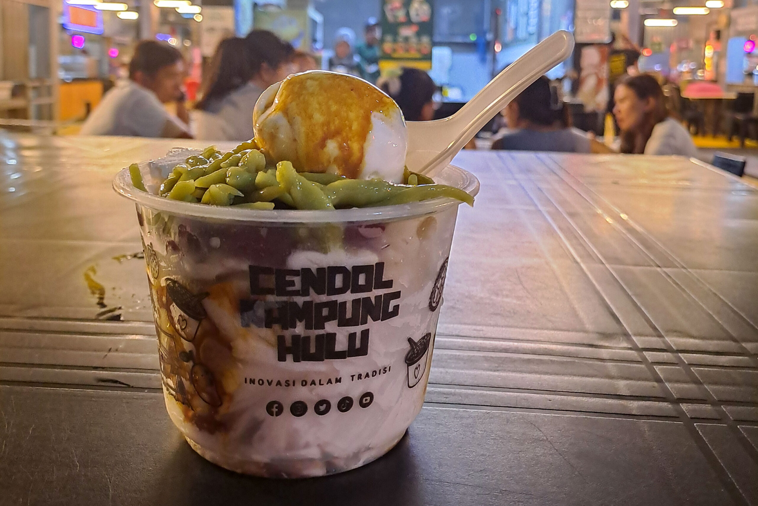 A plastic bowl of cendol with a spoon from Cendol Kampung Hulu 