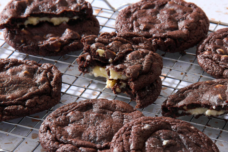 Chocolate cheesecake cookies on a cooling rack, with a few cookies broken open to show the cheesecake filling
